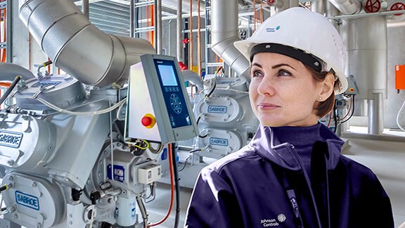 A female technician smiling, with a Sabroe screw comprossor unit in the background