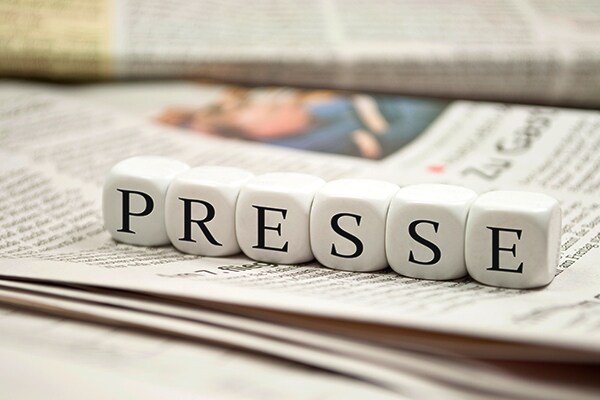 Dice lined up atop a newspaper spelling out P-R-E-S-S-E