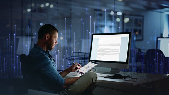 Man using a tablet at his workstation, overlaid with a graphic of transmission nodes in the background
