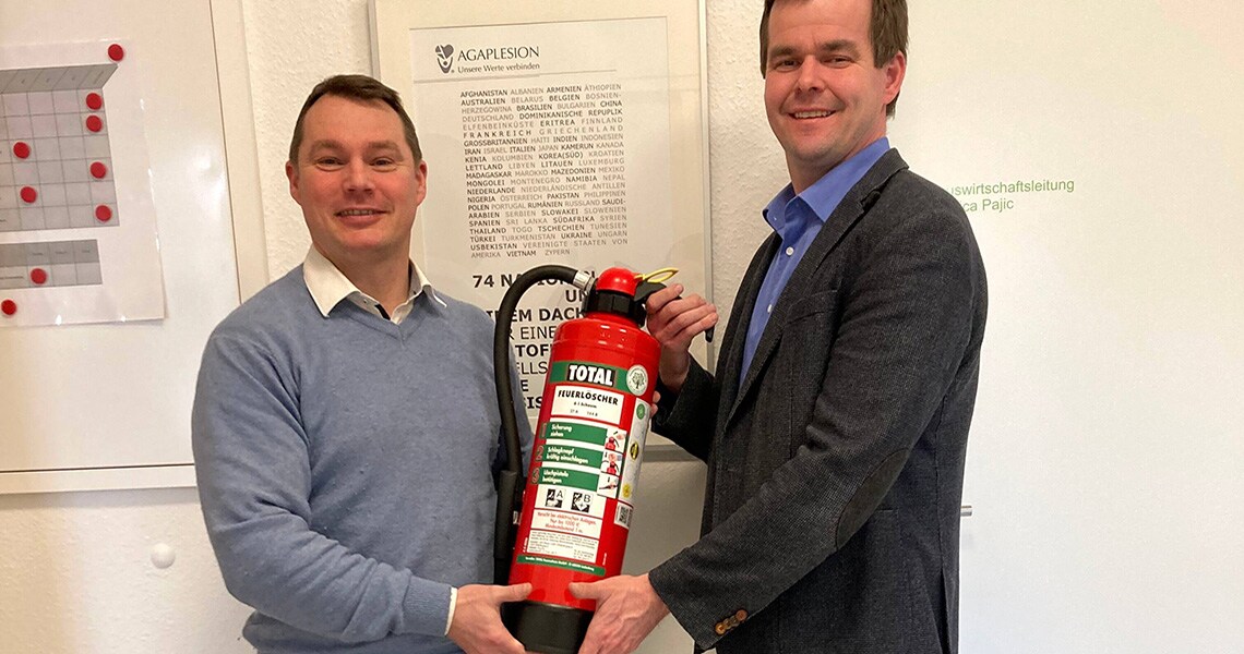 Two people holding a Total fire extinguisher