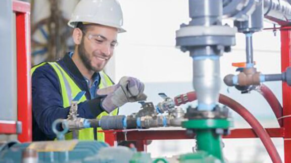 Engineer in safety suit inspecting a gas pipe installed in an indoor space