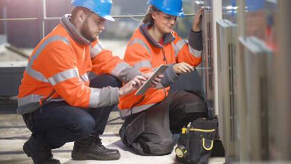 A man and a female engineer in safety suit inspecting a hvac device