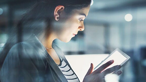 A lady watching the tab closely with blur background of a corporate office
