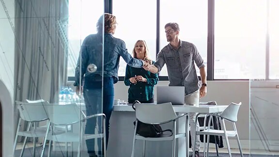 Two men shaking hands while a lady looks on in the corporate office
