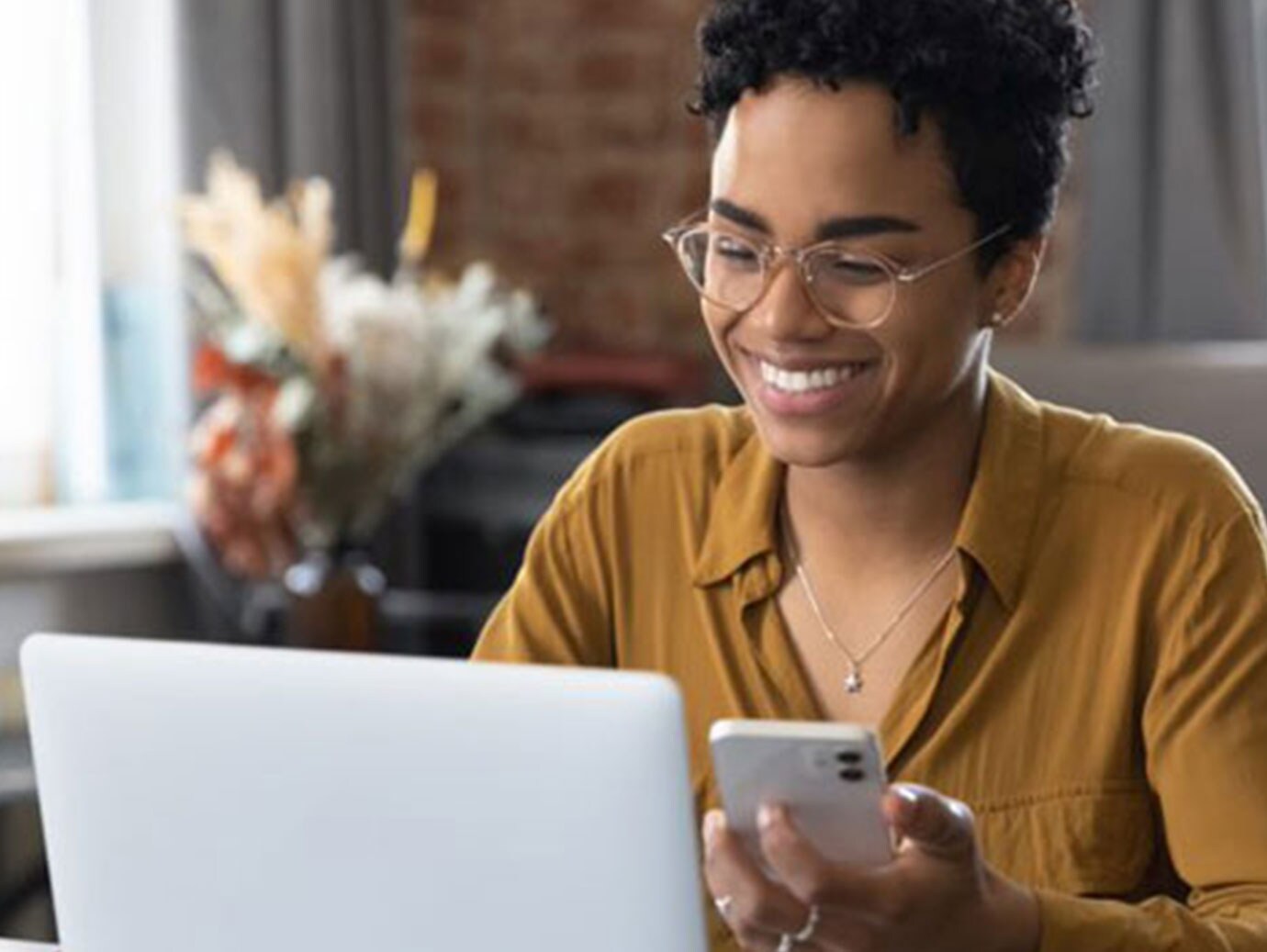 Happy Afro American woman talking on mobile phone with working on laptop at home workplace