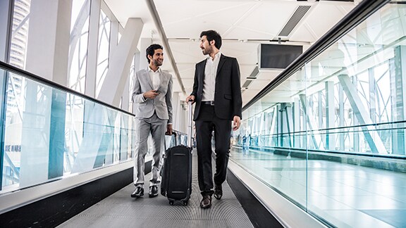 Two men carrying luggage and talking in an airport