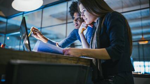 Two female employees discussing work on their desktop 