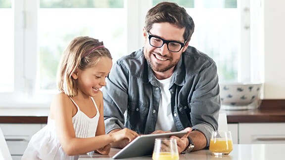 Father and daughter sitting on the dinning table and happily watching the tab