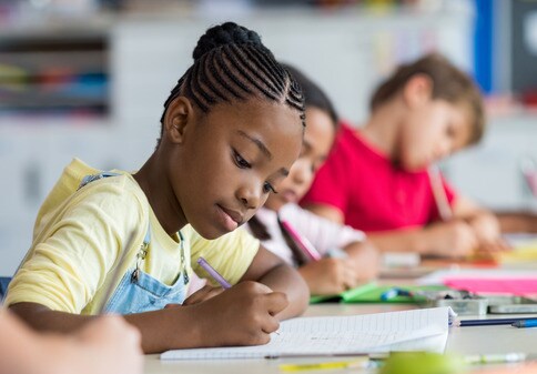 African girl writing in class with blurred background other kids writing 